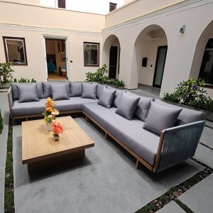 Bộ sofa sân vườn góc L hiện đại với nệm ghi xám, bàn trà gỗ vuông, đặt trong sân biệt thự sang trọng
