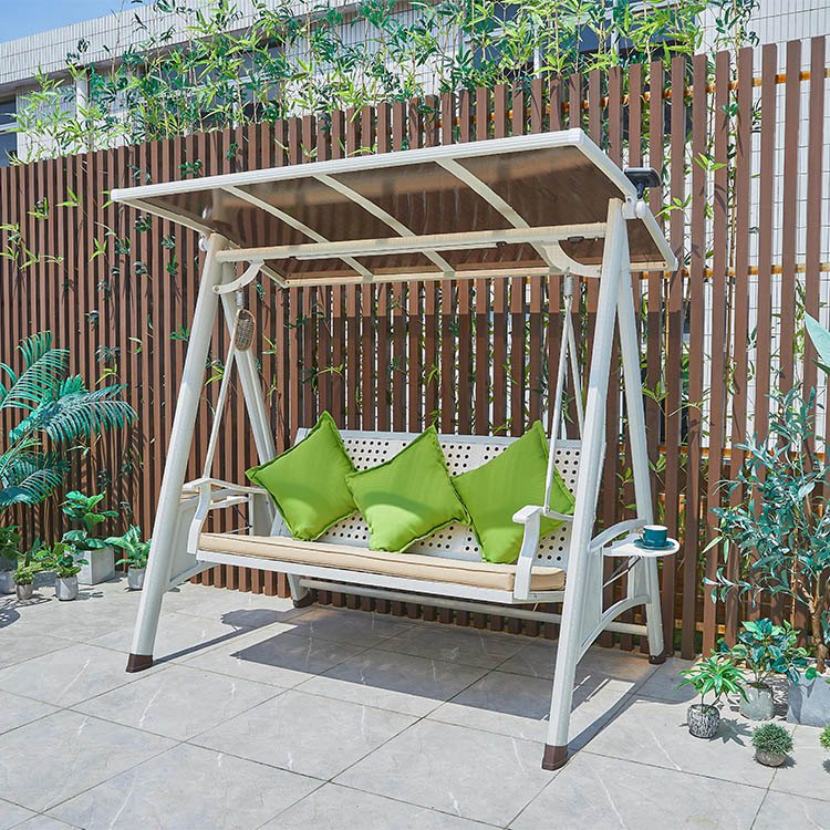 Xích đu sân vườn 3 chỗ khung nhôm trắng, có mái che, nệm be và gối xanh lá, đặt ngoài trời