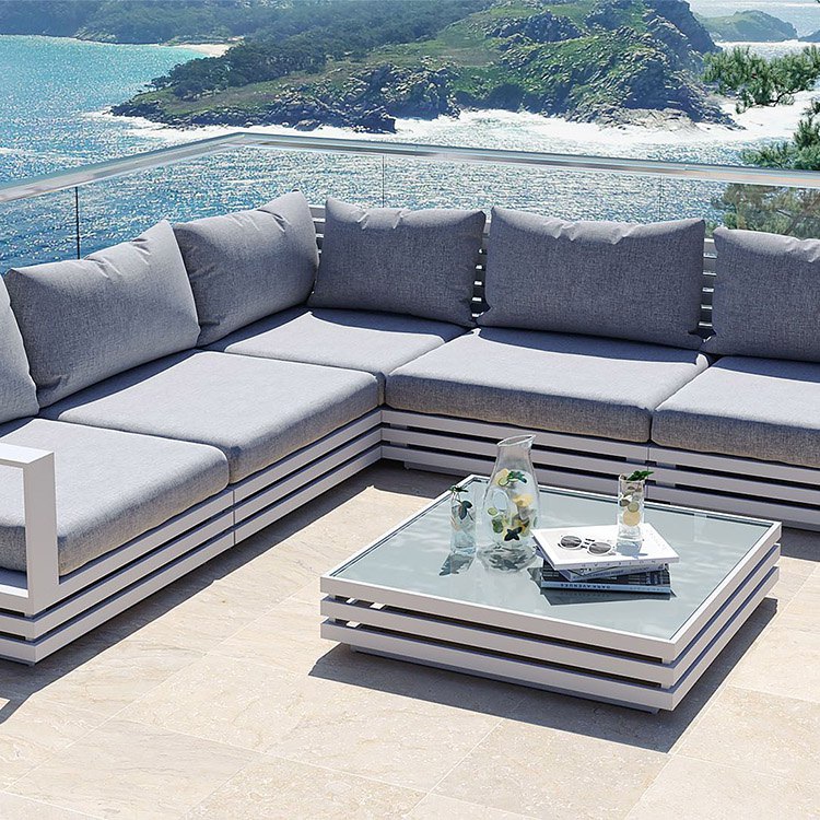 Bộ sofa ngoài trời chữ L màu trắng, nệm xám, bàn trà kính, view biển sang trọng