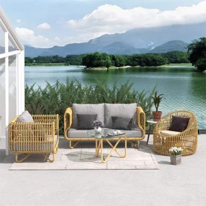 Bộ sofa ngoài trời giả mây màu vàng nhạt, nệm ghi, đặt cạnh hồ nước, gồm sofa đôi, 2 ghế đơn, bàn kính