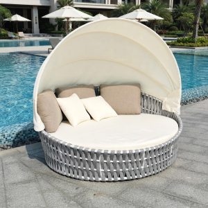 Giường tắm nắng tròn ngoài trời đặt cạnh hồ bơi khách sạn, nệm kem và gối tựa sang trọng
