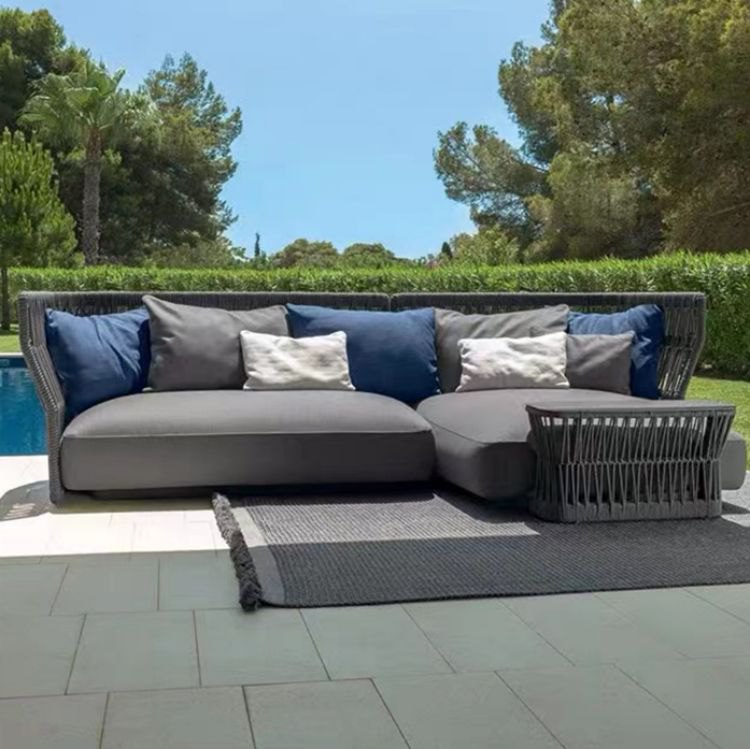 Sofa ngoài trời màu xám đậm, nệm dày, gối tựa xanh phối trắng, bàn trà đồng bộ, đặt cạnh hồ bơi sang trọng