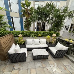 Sofa sân vườn khung nhôm, dây rope xám, nệm trắng, đặt ngoài trời gần cây xanh và bàn dài