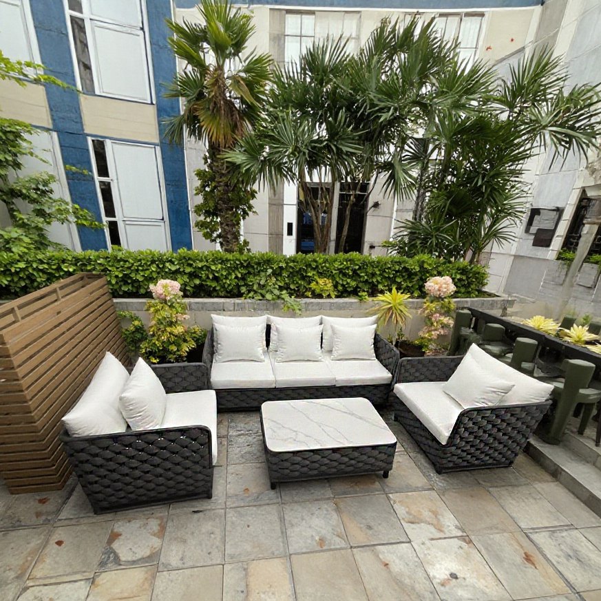 Sofa sân vườn khung nhôm, dây rope xám, nệm trắng, đặt ngoài trời gần cây xanh và bàn dài