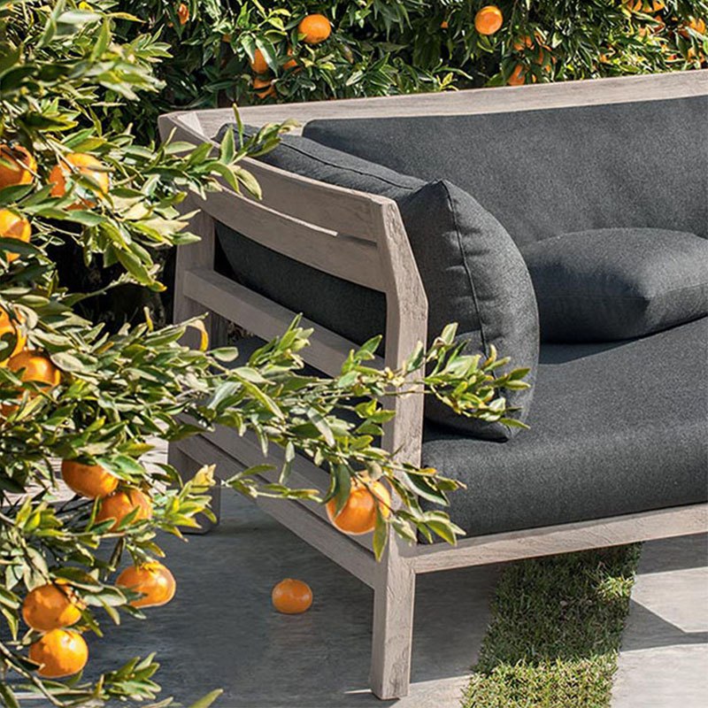 Cận cảnh sofa góc L khung gỗ teak, nệm xám đậm, đặt giữa vườn cây cam