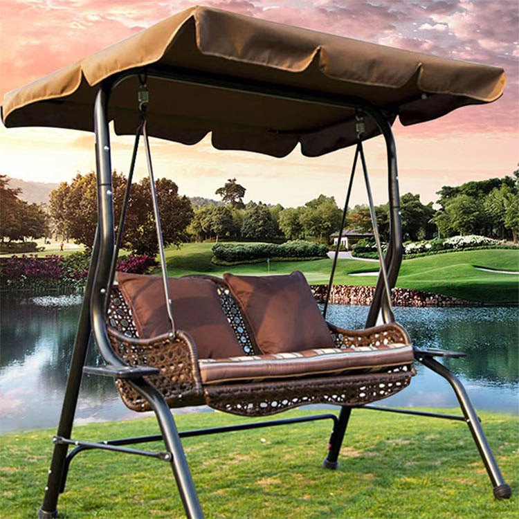Xích đu giả mây ngoài trời, nệm nâu, gối sọc, mái che nâu, đặt trên bãi cỏ cạnh hồ golf
