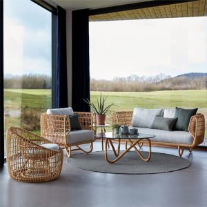 Bộ sofa sân vườn giả mây gồm sofa đôi, 2 ghế đơn, bàn trà kính, nệm ghi, bối cảnh phòng khách view đồng cỏ