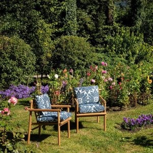 Hai ghế đơn sofa ngoài trời khung gỗ teak, nệm vải họa tiết xanh dương nổi bật giữa vườn hoa