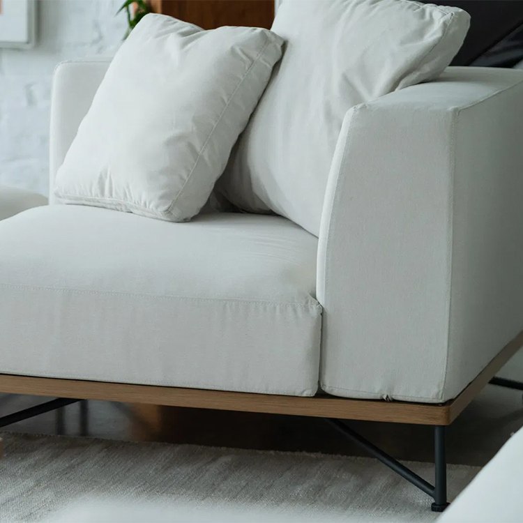 Cận cảnh ghế sofa đơn với nệm dày và gối tựa màu trắng kem, khung chân nhôm chắc chắn
